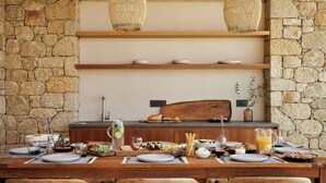 A rustic stone wall with a wooden table set for breakfast, including plates, glasses, and a pitcher of orange juice.