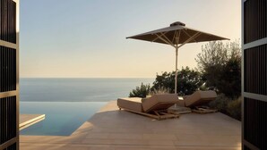 An infinity pool with lounge chairs and an umbrella, overlooking a clear horizon.
