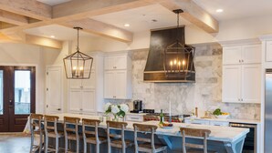 A spacious kitchen with white cabinets, a large island with bar stools, and a stone backsplash. - Sleeps 48, 2 Homes w/ Private Beach Access | Bradley Circle Buyout by AvantStay (Hilton Head Island)