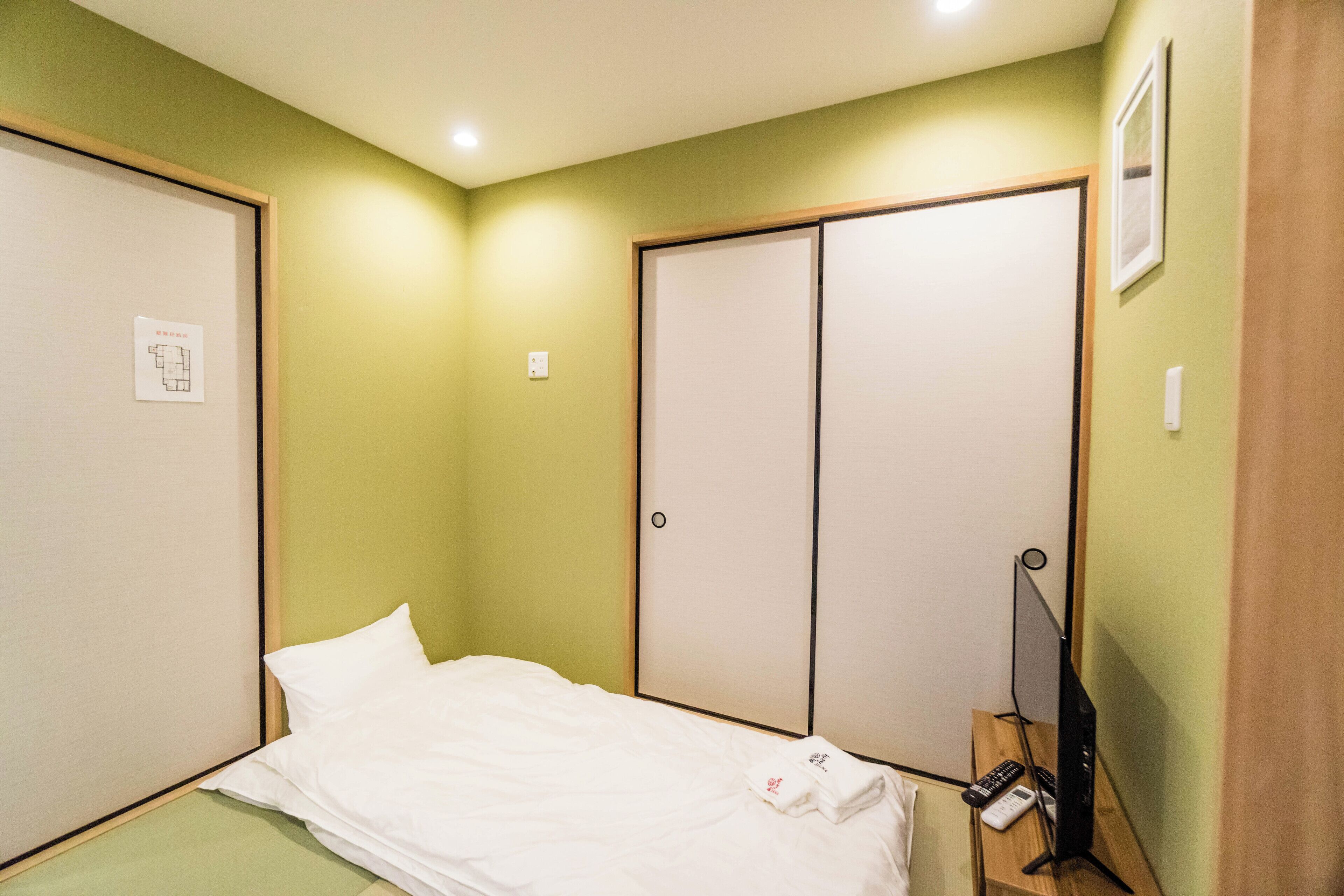 A bedroom with a bed, a wardrobe, and a desk with a television and remote control.