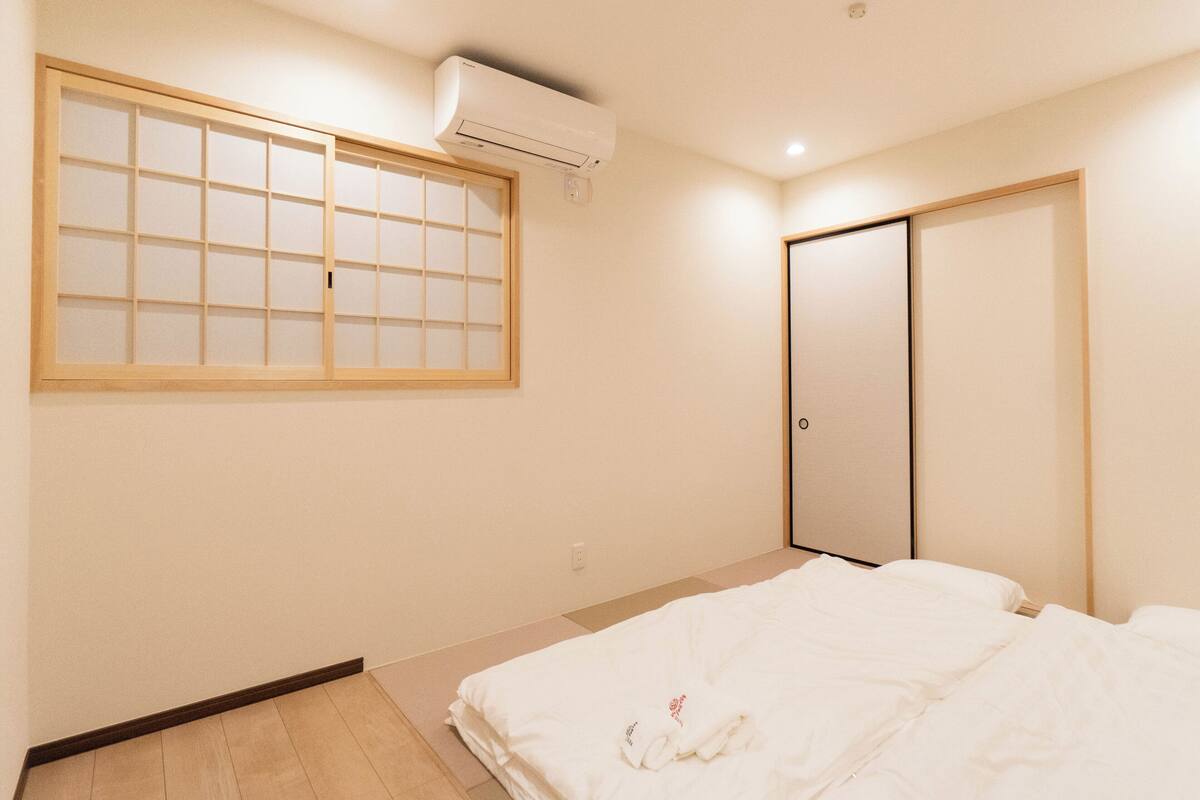 Ein Hotelzimmer mit Bett, einem Fenster mit Holzrahmen, einer Klimaanlage und einer Schiebetür.