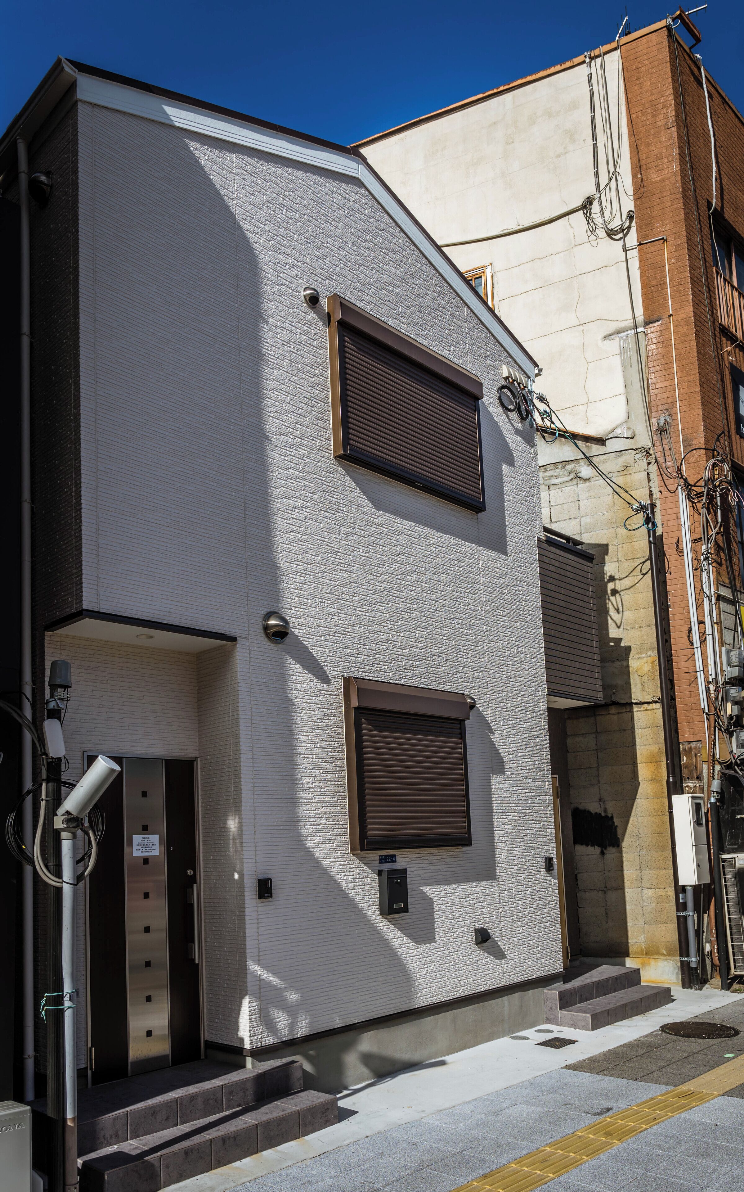 A modern building with a white textured facade, two brown-framed windows, and a visible elevator.
