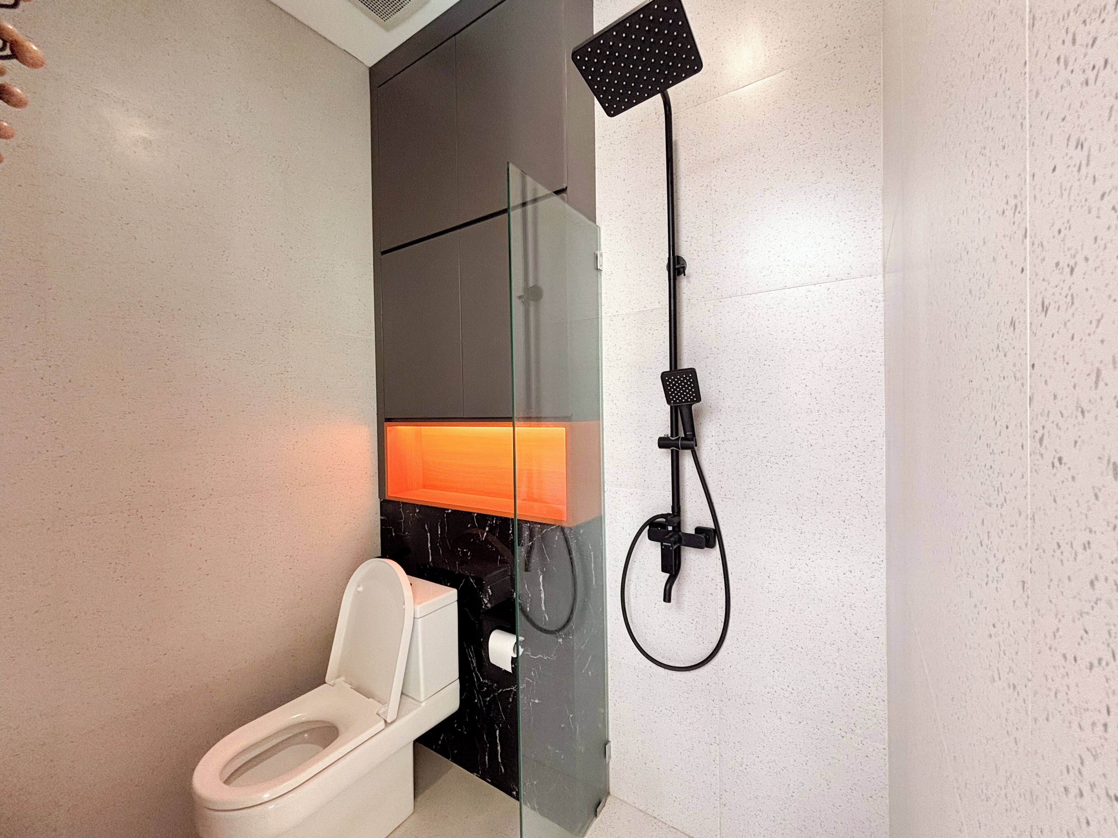 Moderni kylpyhuone, jossa on lasinen suihkuseinä, wc ja seinälle kiinnitetty pyyhekoukku.