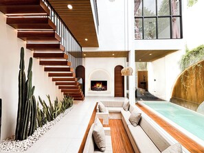 A modern interior with a wooden staircase, a seating area, and a pool. - Villa Kelana Jimbaran (Jimbaran)