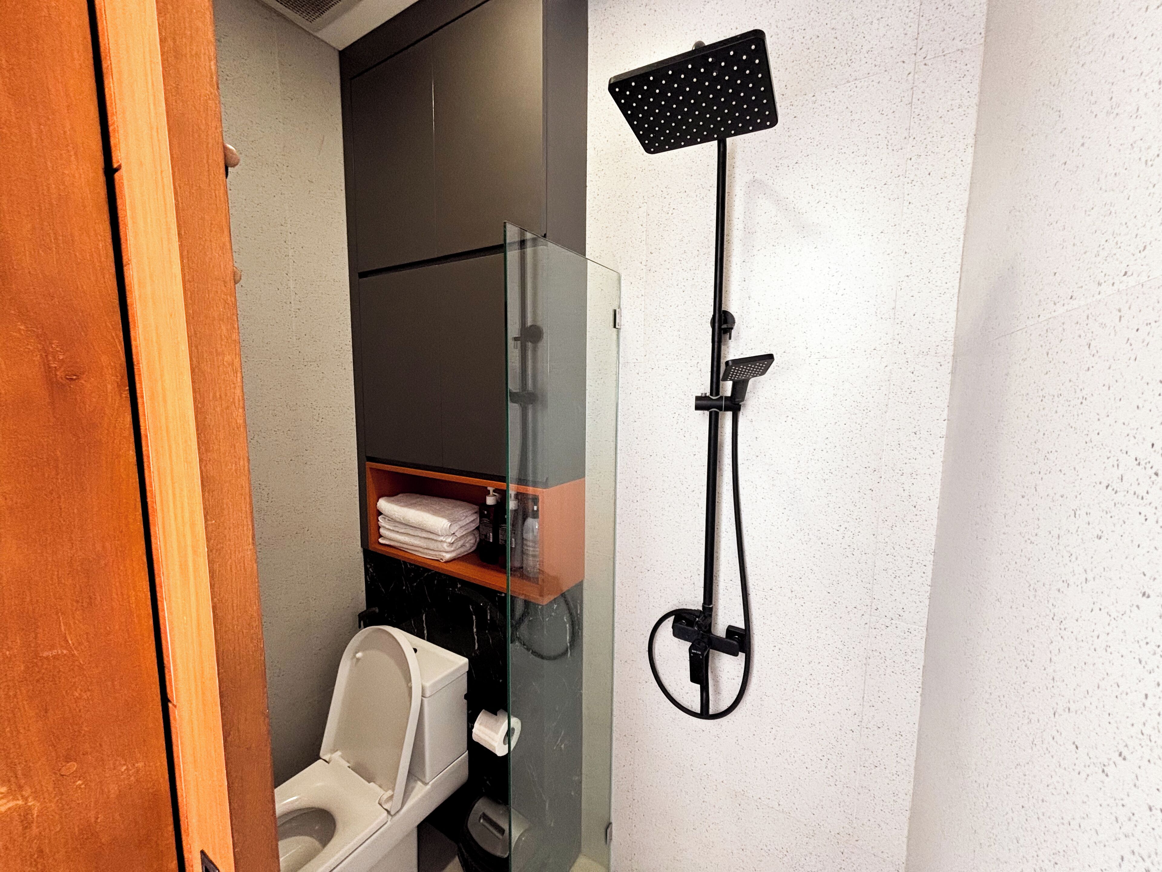 Ein Badezimmer mit Toilette, einer Duschkabine und einem Ablagefach mit gefalteten Handtüchern.