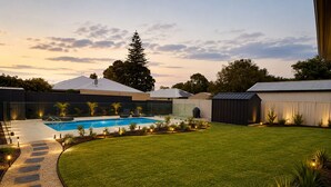 Un patio trasero con piscina, césped cuidado y un camino que lleva a la piscina.