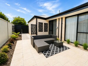 Un patio moderno al aire libre con una zona de estar integrada, un sendero y un pequeño jardín.