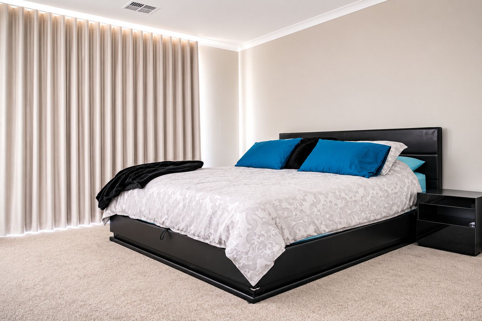 A modern bedroom with a black bed frame, white bedding, and blue pillows.