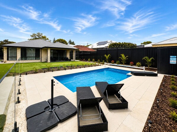 A swimming pool with lounge chairs, a patio area, and a house in the background.