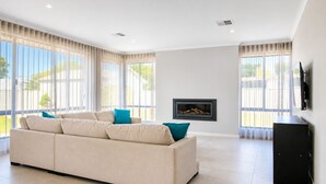 Una sala moderna con un sofá color beige, una chimenea y ventanas grandes.