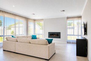 Una sala moderna con un sofá color beige, una chimenea y ventanas grandes.