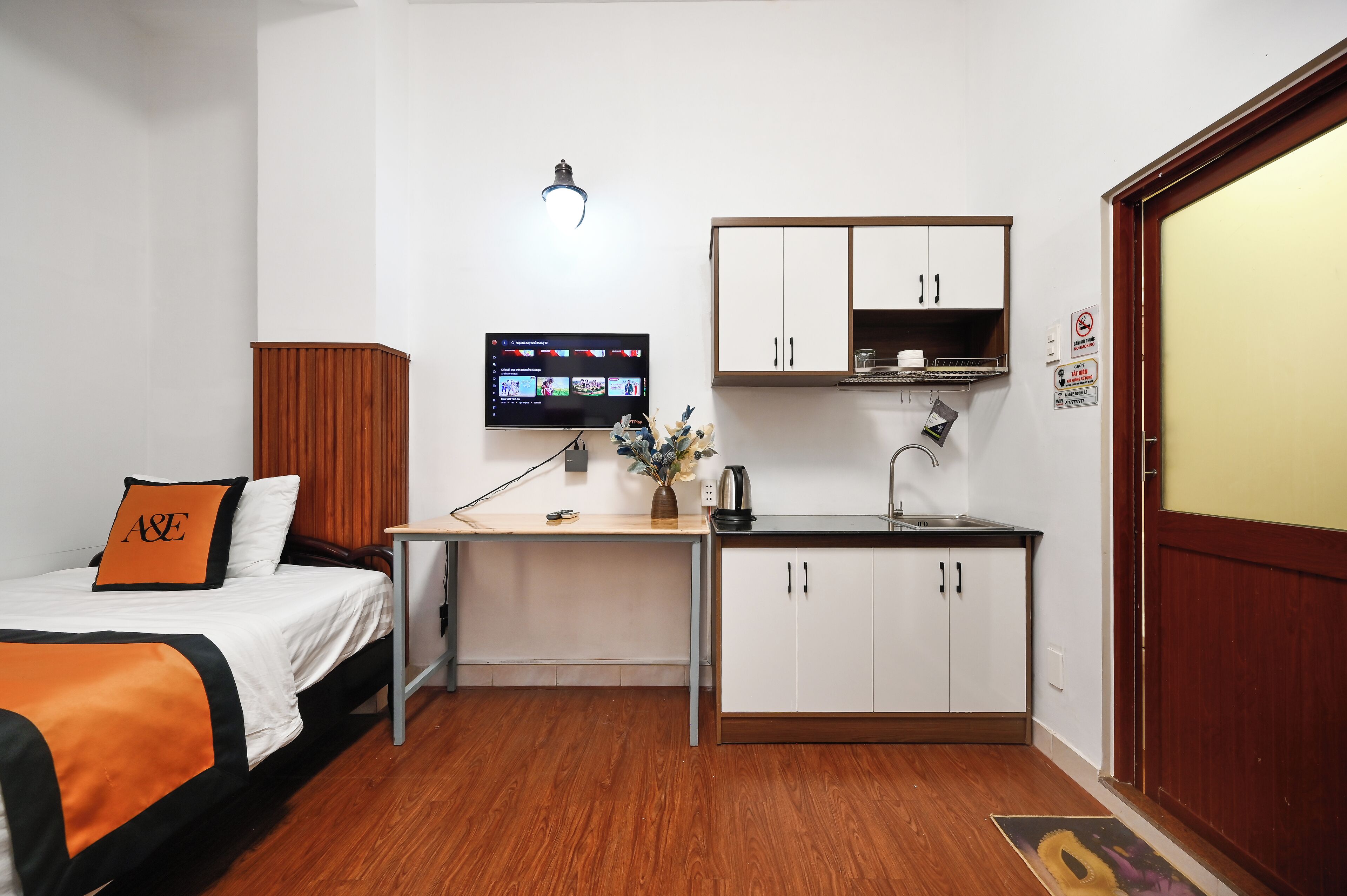 A compact hotel room with a bed, a desk with a computer, a kitchenette, and a wardrobe.