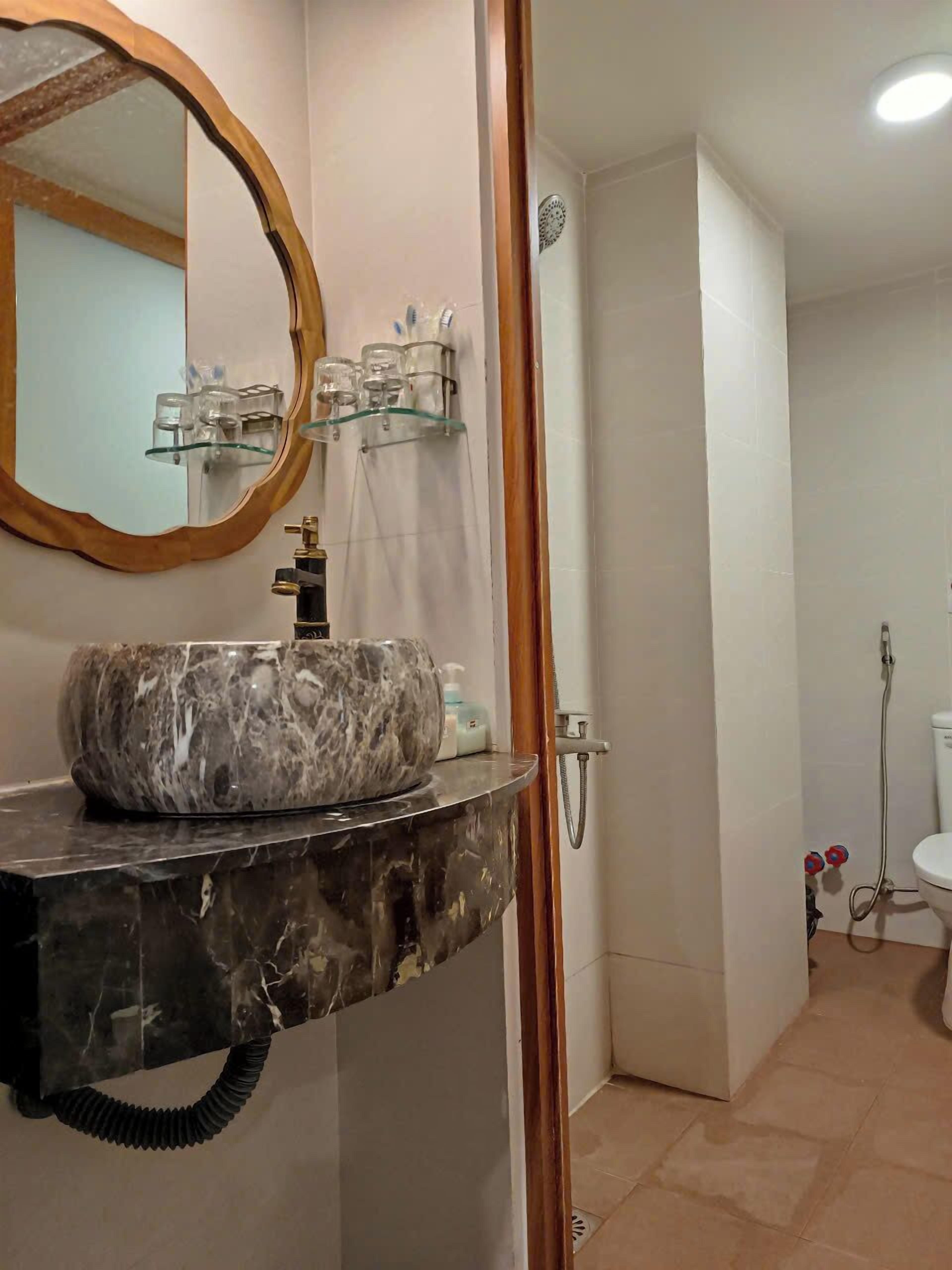 A bathroom with a marble sink, a round mirror, and a glass shelf with toiletries.