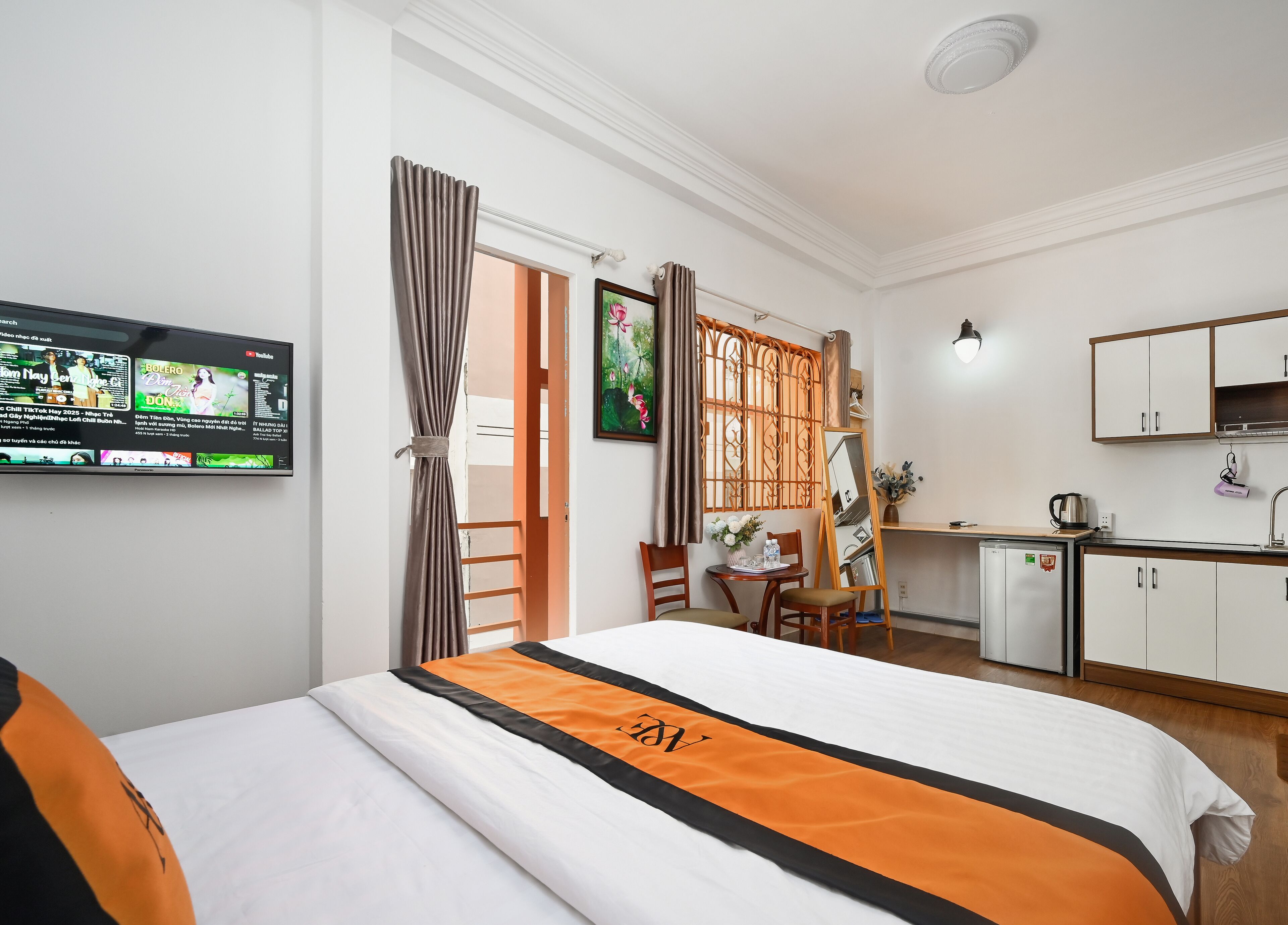 Habitación de hotel con cama, escritorio con computadora, kitchenette pequeña y televisor en la pared.