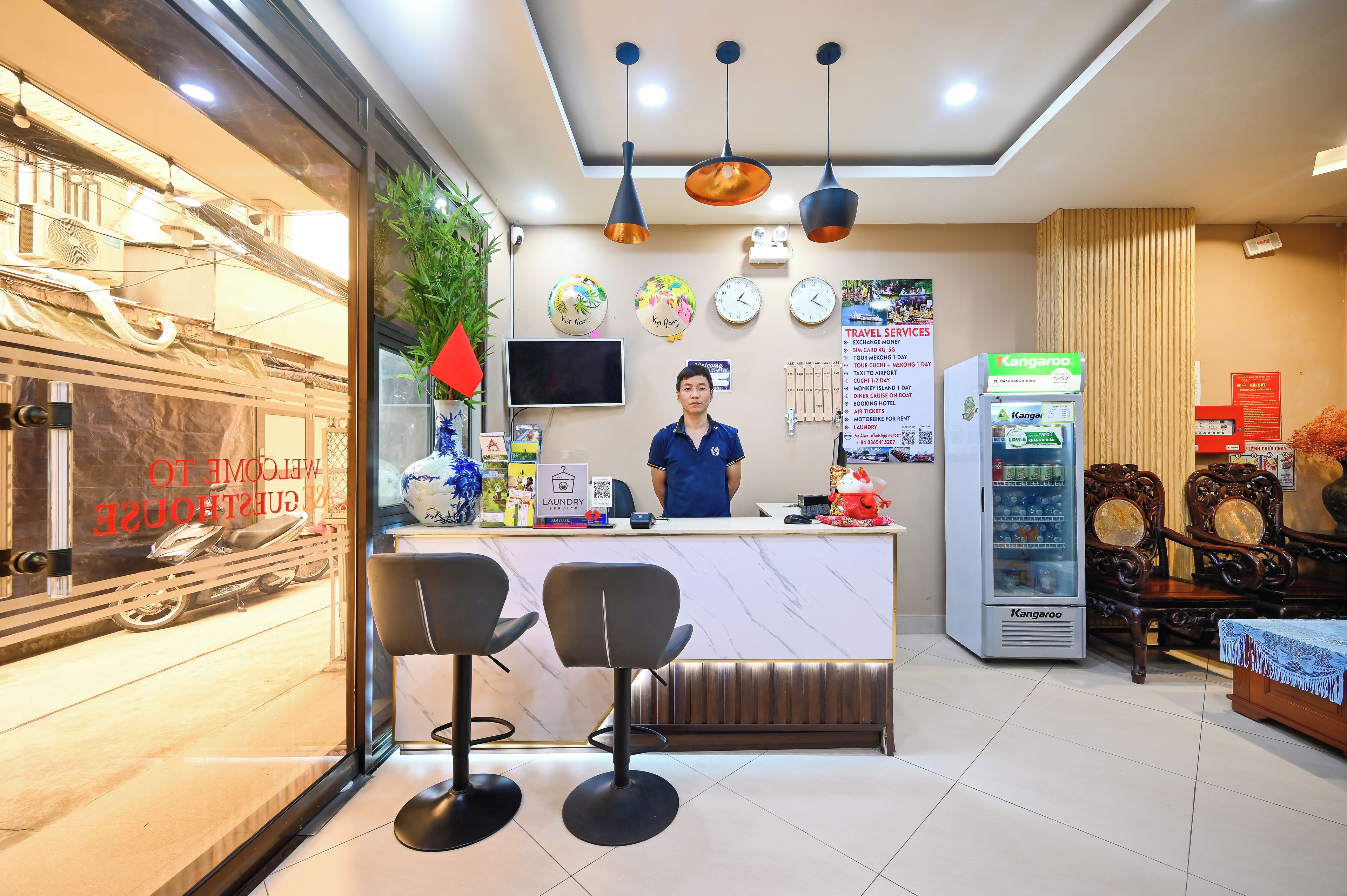 A hotel reception area with a counter, two bar stools, a Kangaroo vending machine, and a wall clock.