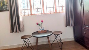 A room with a wooden floor, a round table with two chairs, a cabinet, and a window with curtains. - A&E GuestHouse (Ho Chi Minh City)