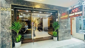 A hotel entrance with a marble facade, a reception desk, and two potted plants. - A&E GuestHouse (Ho Chi Minh City)