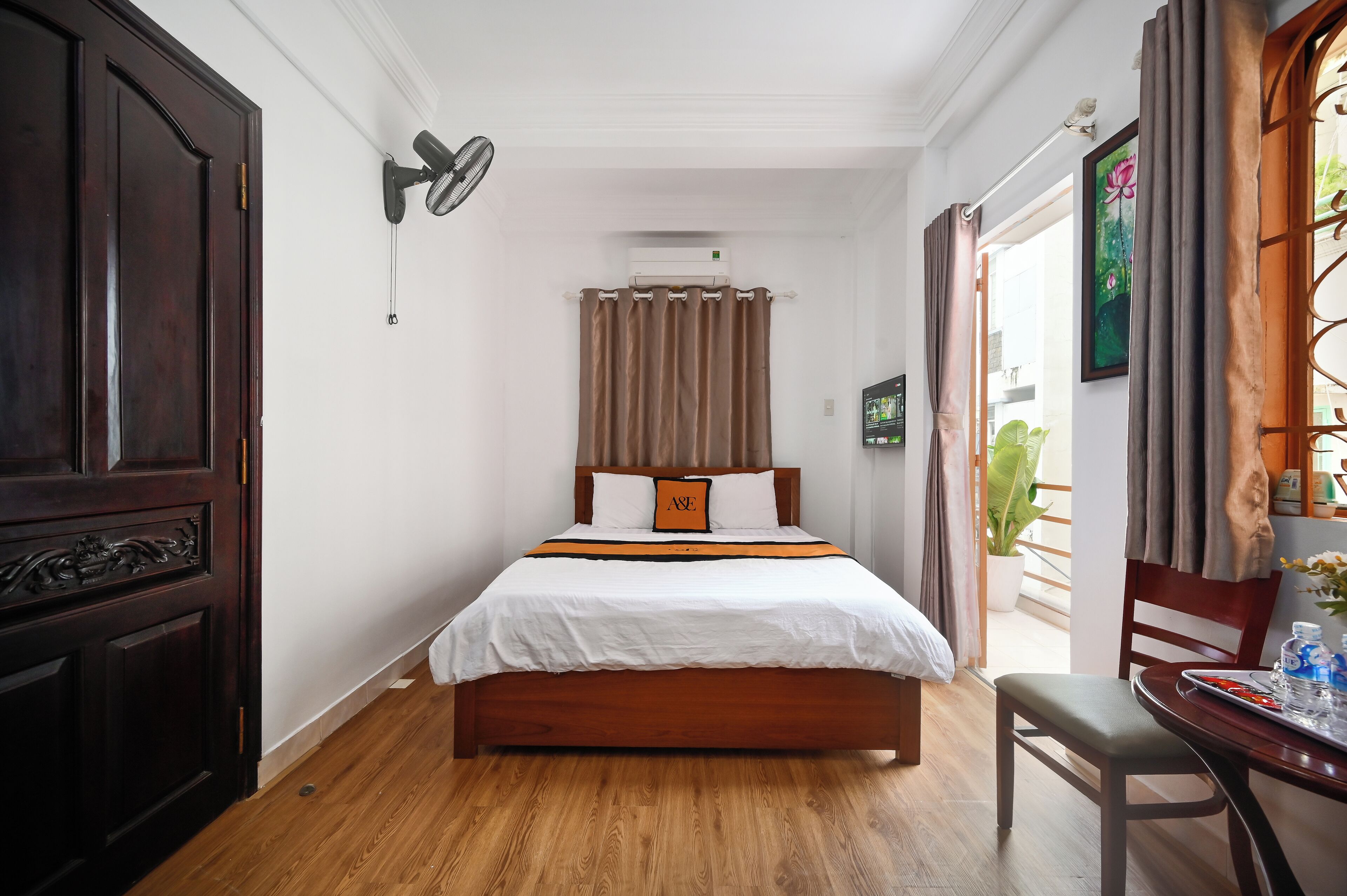 Hotelkamer met een houten bed, een plafondventilator, een airconditioning en een raam met gordijnen, met uitzicht op de omgeving.
