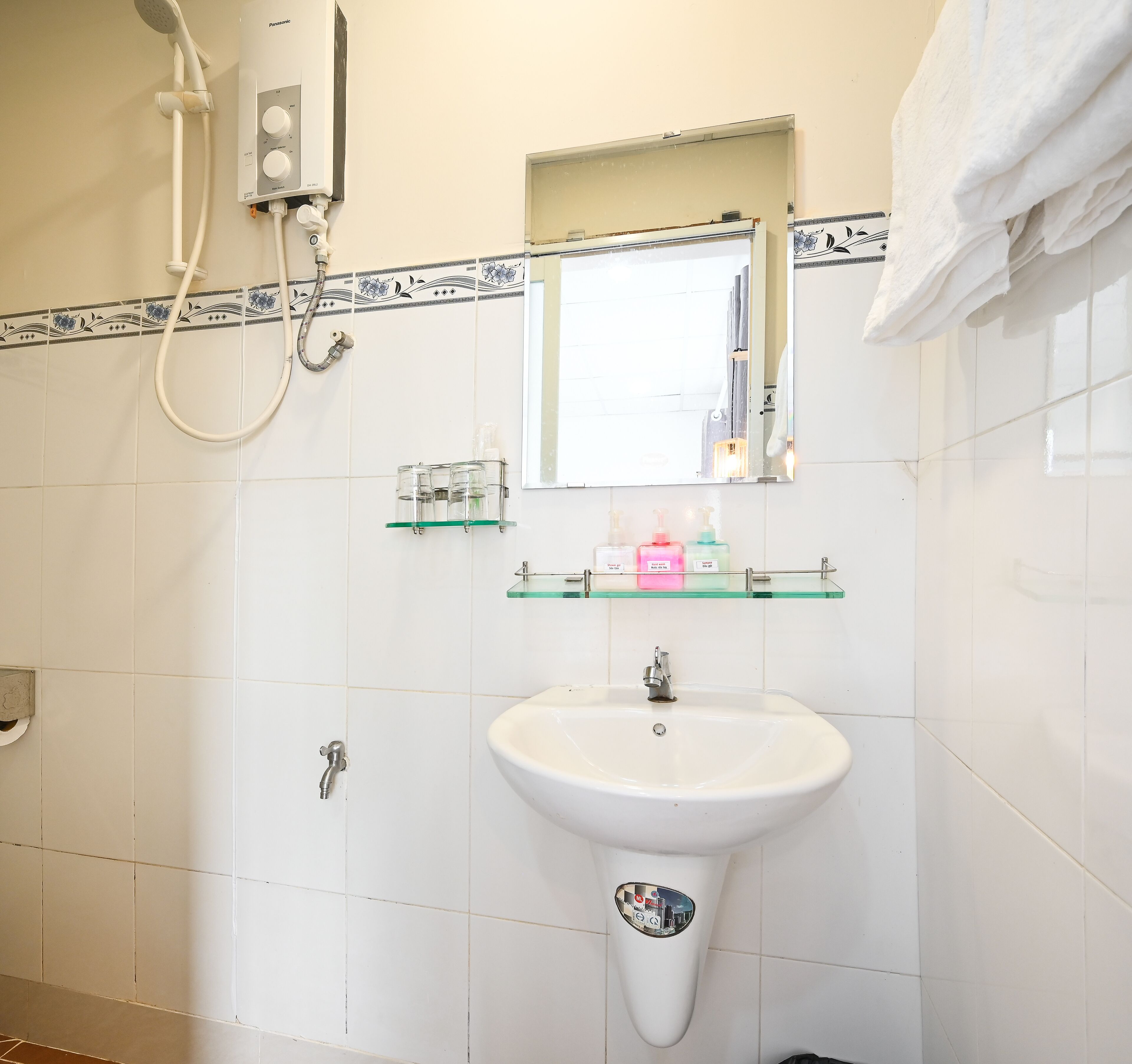 A bathroom with a white sink, a mirror, and a shower. There are toiletries on the wall and a towel hanging on the right.