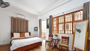 A hotel room with a wooden bed, a small table with chairs, a whiteboard, and a view through a window with curtains. - A&E GuestHouse (Ho Chi Minh City)