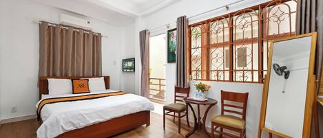 A hotel room with a wooden bed, a small table with chairs, a whiteboard, and a view through a window with curtains.