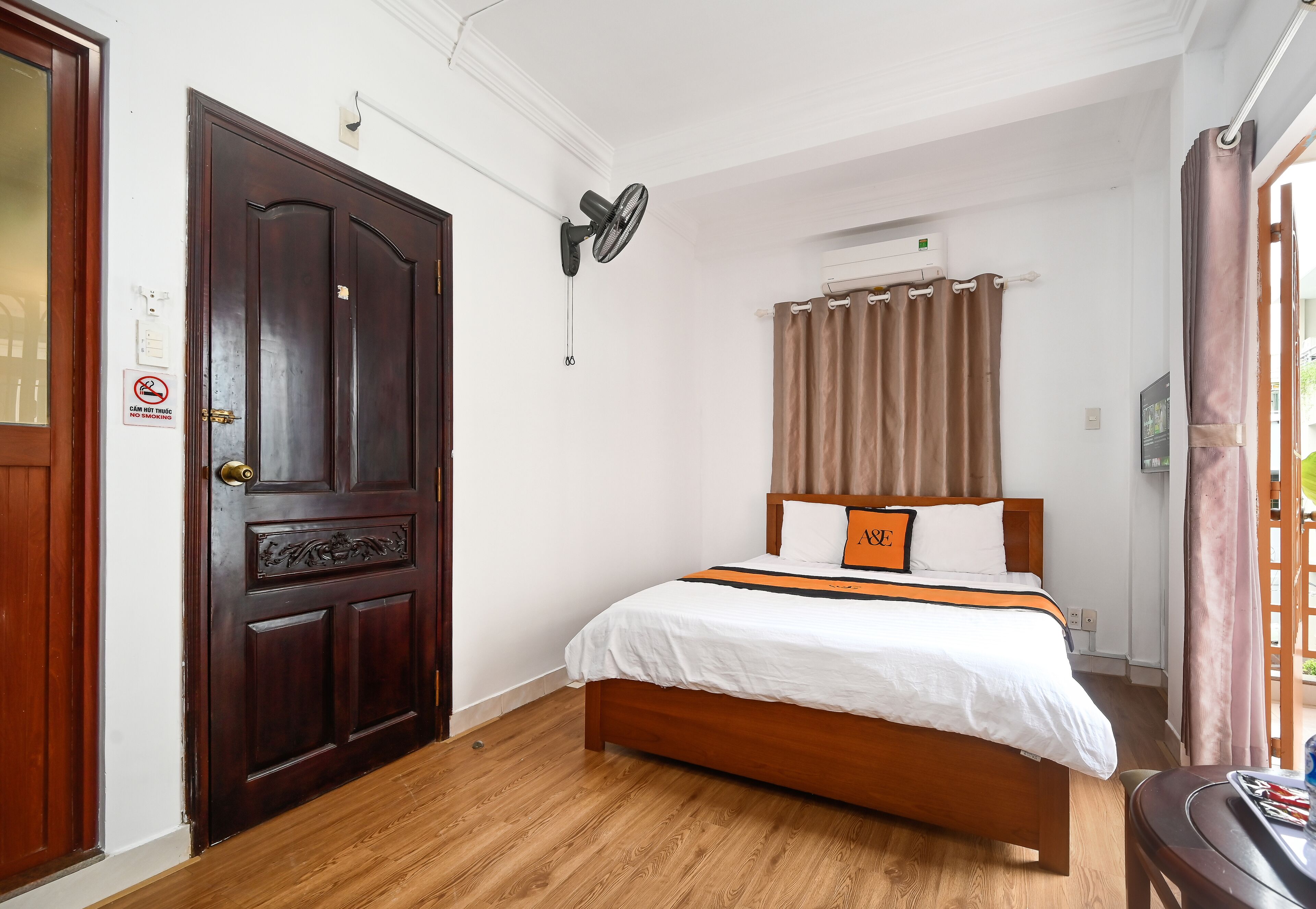A bedroom with a wooden bed, a ceiling fan, a window with curtains, and a door with a no-smoking sign.