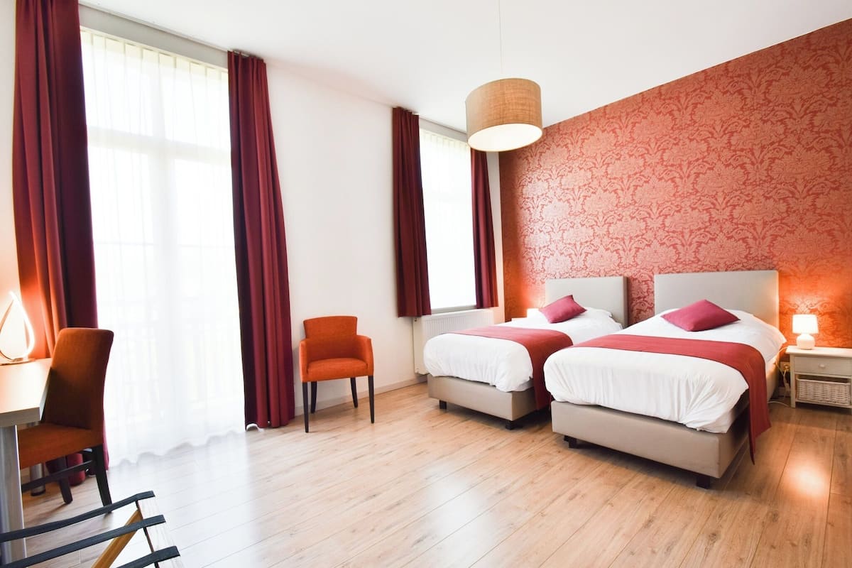 A hotel room with two beds, a desk, a chair, and a window with curtains.