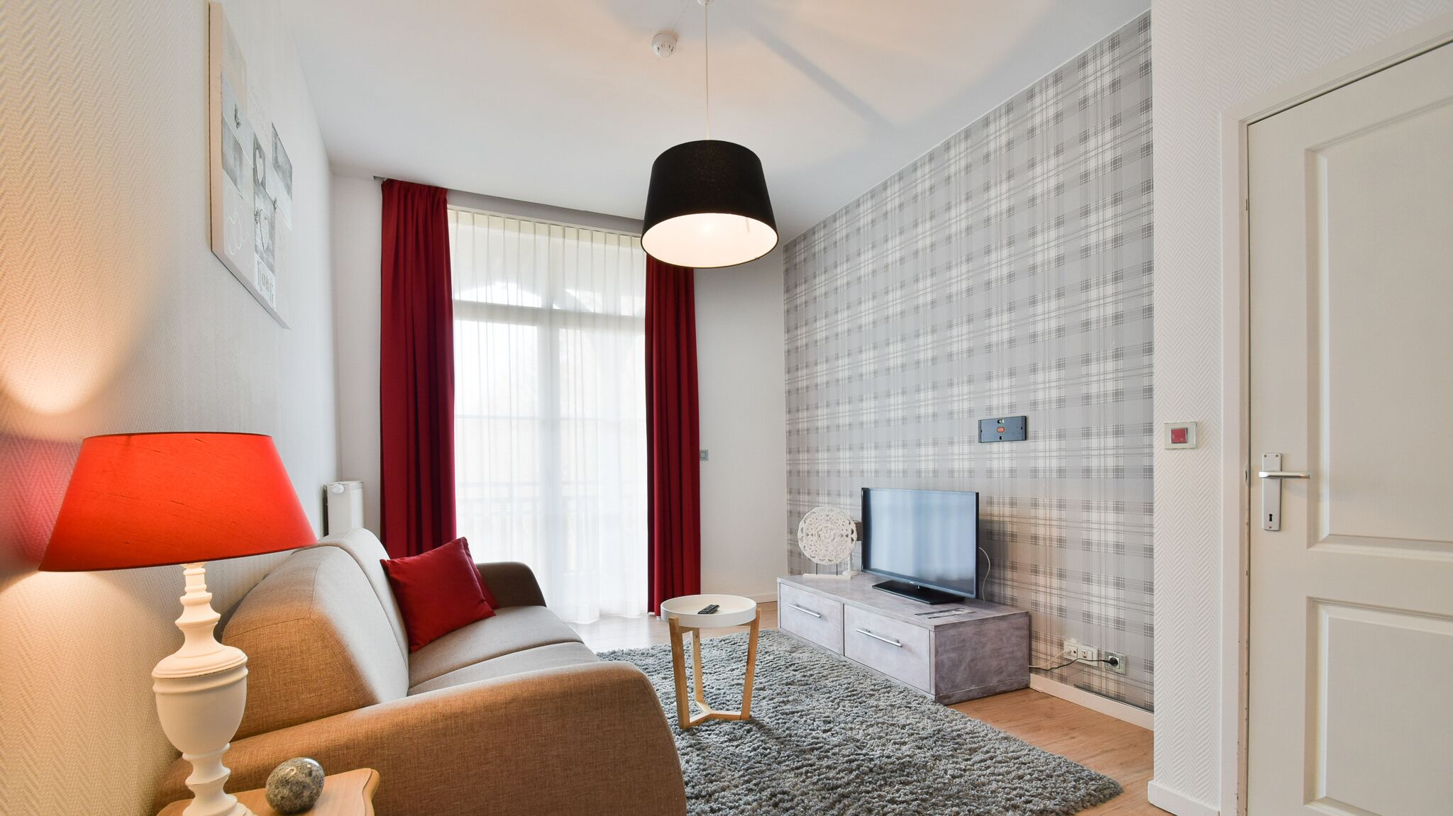 A modern living room with a sofa, a TV, a lamp, and a red curtain.