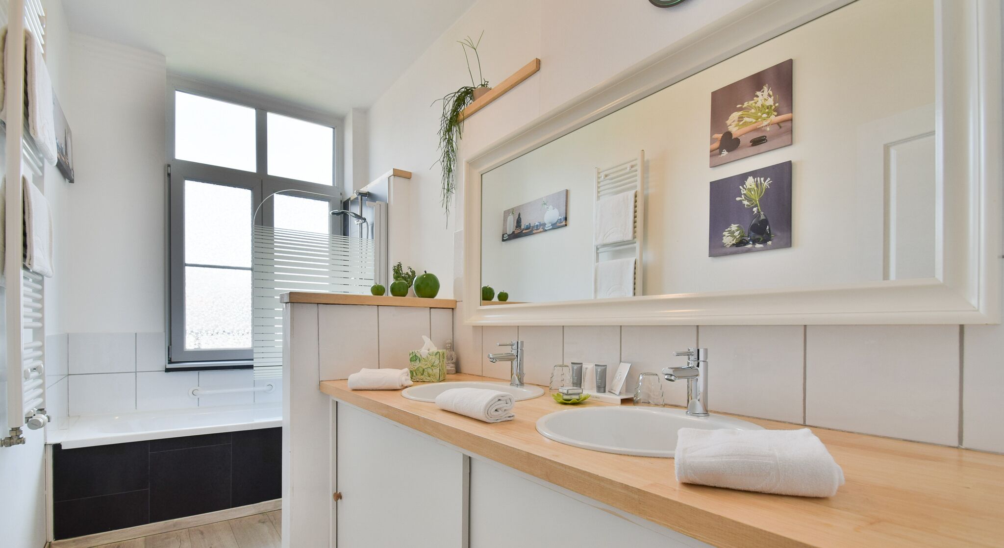 Une salle de bain moderne avec un grand miroir, deux lavabos et une fenêtre équipée de stores.