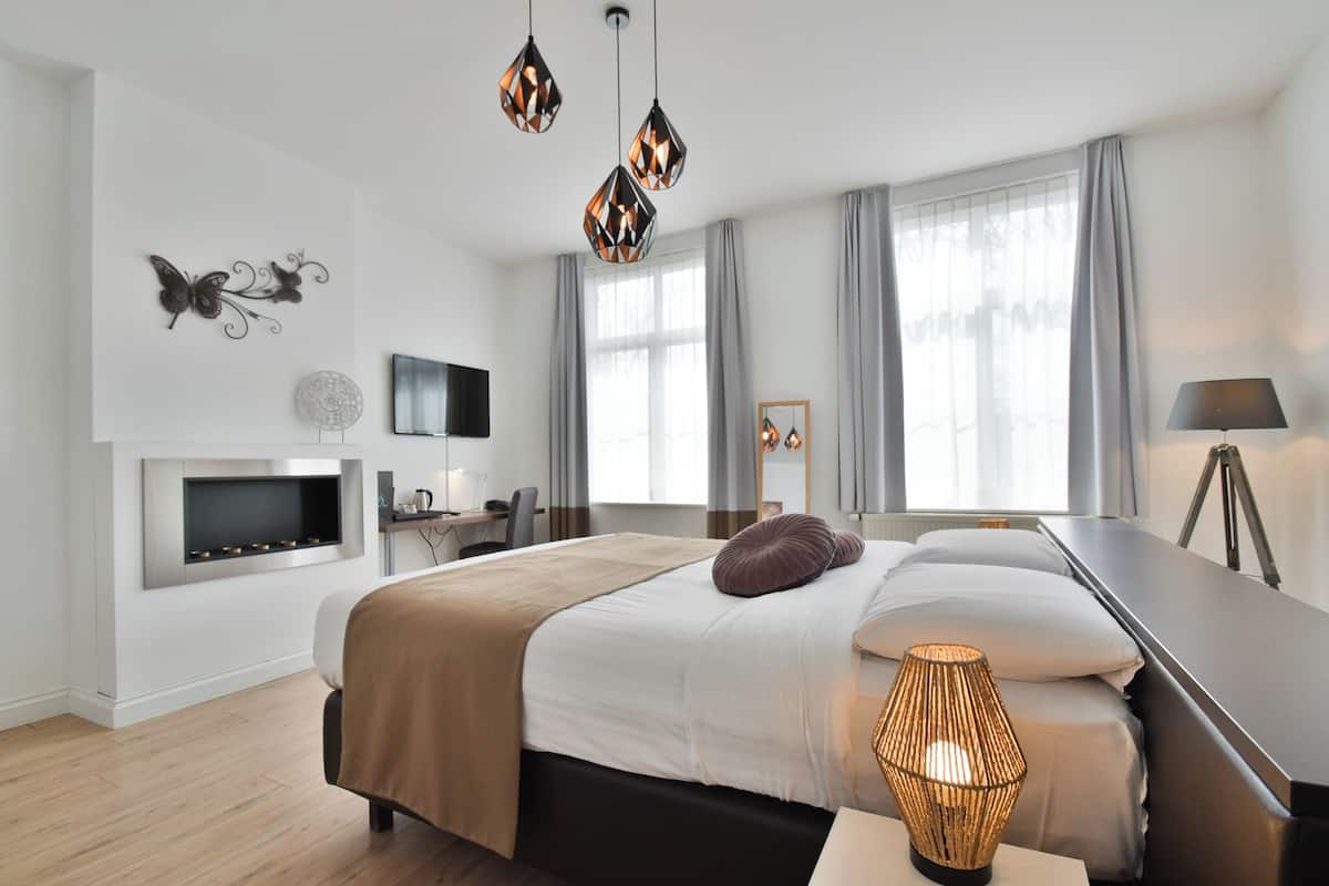 A modern hotel room with a large bed, a desk, a flat-screen TV, and a fireplace.