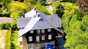 Een ruim, twee verdiepingen tellend huis met een opvallend balkon, omringd door weelderige begroeiing en een verzorgd gazon.