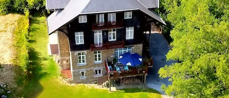 A large, two-story house with a prominent balcony, surrounded by lush greenery and a well-maintained lawn.