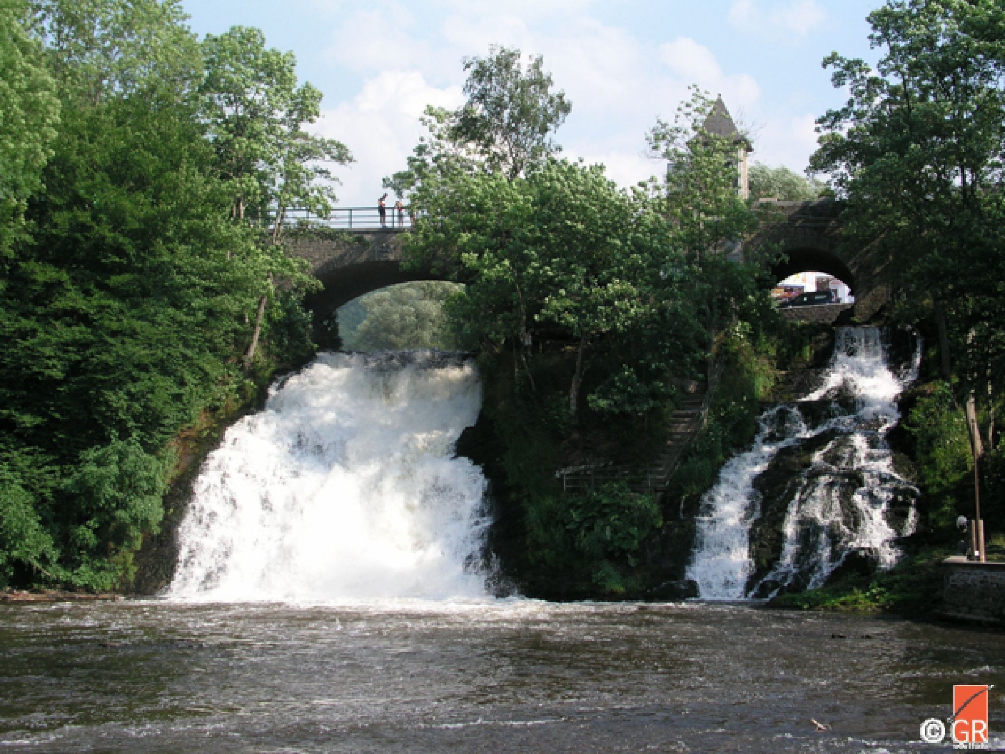 Een brug over een rivier met een waterval, omringd door groen.