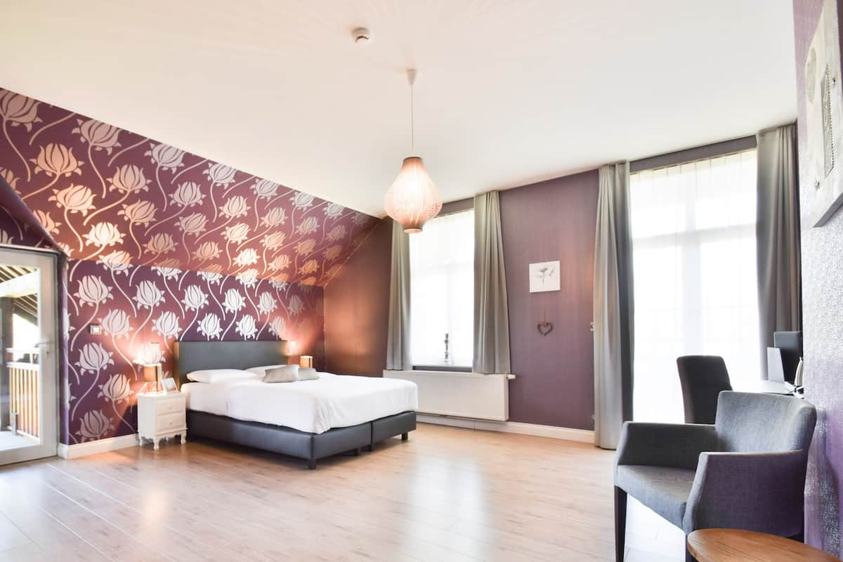 A modern bedroom with a large bed, a nightstand, a desk, and a chair. There is a window with curtains and a view of the outside.