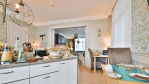Een goed verlichte keuken met een eethoek, met een houten tafel voor twee personen, een kroonluchter en een uitzicht op de eetkamer.