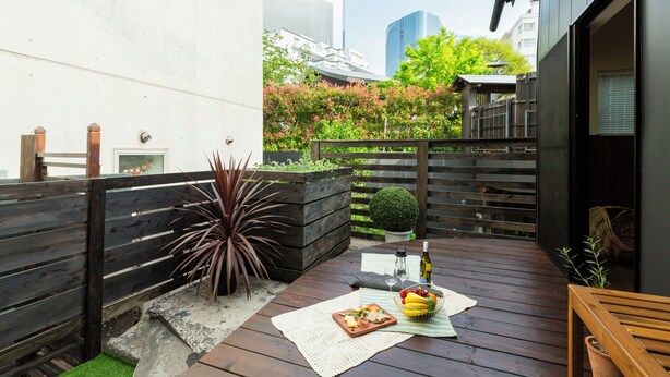 A wooden deck with a table set for a meal, surrounded by a wooden fence and a small garden. - HOTEL RIN TOKYO (Tokyo)
