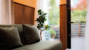 A sofa with cushions, a potted plant, and a view through a door to an outdoor area with a wooden deck. - HOTEL RIN TOKYO (Tokyo)