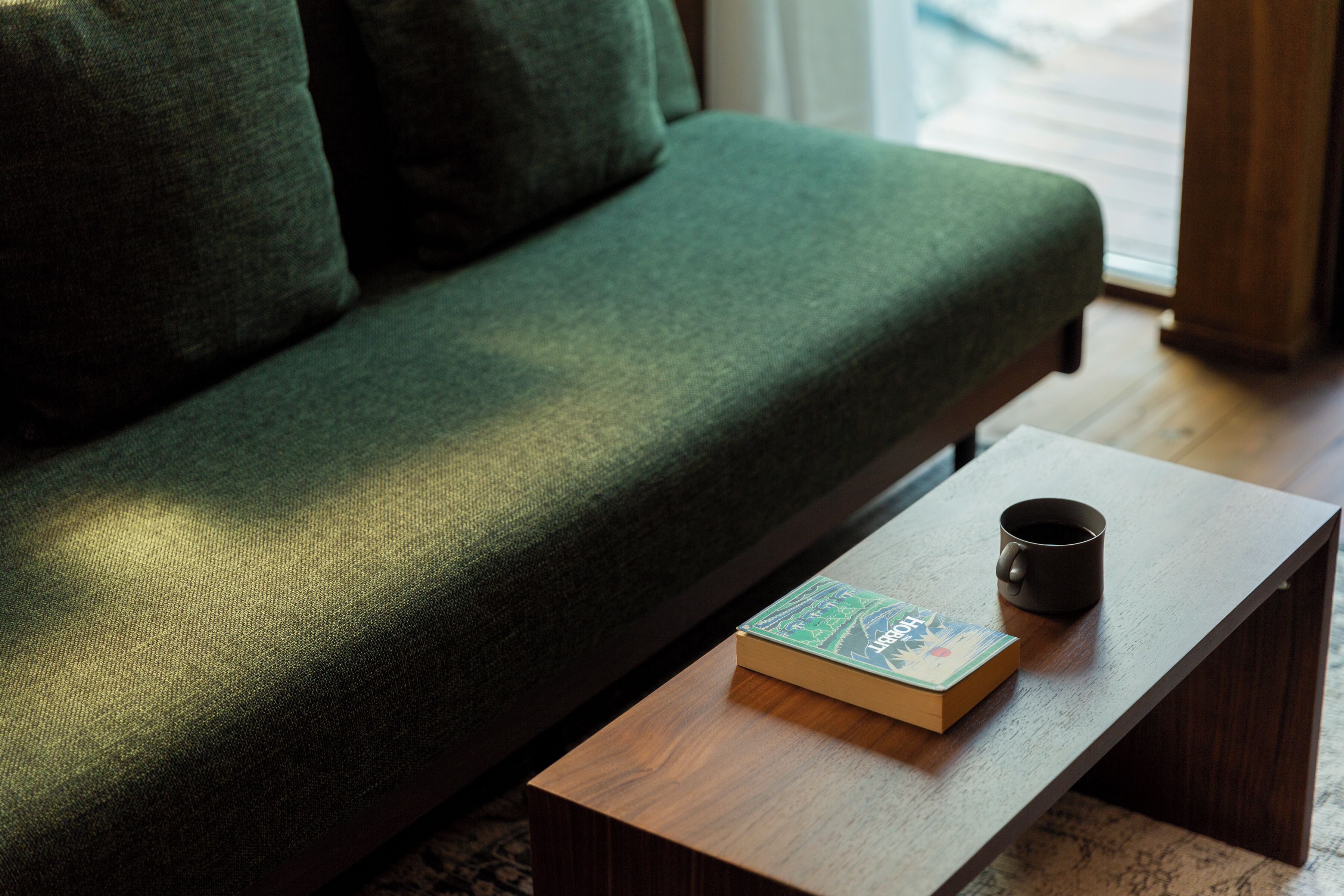 A green sofa with a wooden coffee table in front, a book, and a black mug on the table.