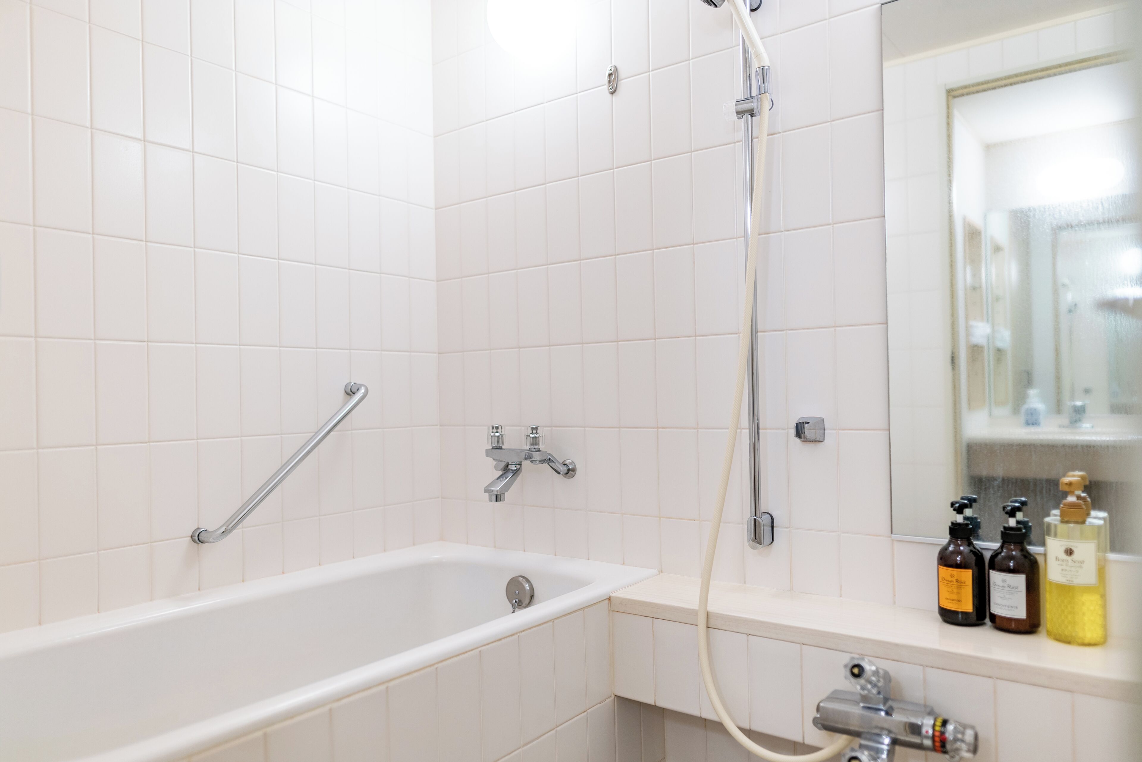 A bathroom with a white bathtub, a shower, and a sink. There are toiletries on the sink counter.