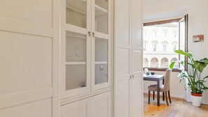 A room with a dining area, a potted plant, and a view of a building through an open door. - Elegant & Cozy Apartment Florence City Center (Firenze)