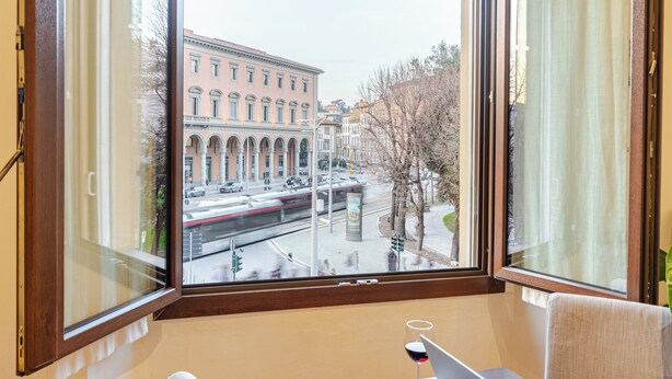 A room with a large window offering a view of a train passing by, a laptop on a table, and a glass of red wine. - Elegant & Cozy Apartment Florence City Center (Firenze)