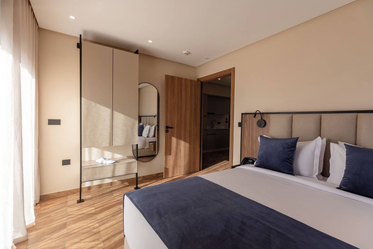 A modern bedroom with a large bed, a wardrobe, and a mirror.