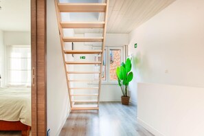 A modern hotel room with a wooden staircase, a bed, a potted plant, and a window with a view of a brick building. - Cozy Ostend Home Tin Tin la Mer Near Beach (Ostend)