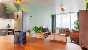 Eine moderne Küche mit einem Edelstahlkühlschrank, ein Essbereich mit Holztisch und -stühlen sowie ein Wohnzimmer mit Sofa und Fernseher.