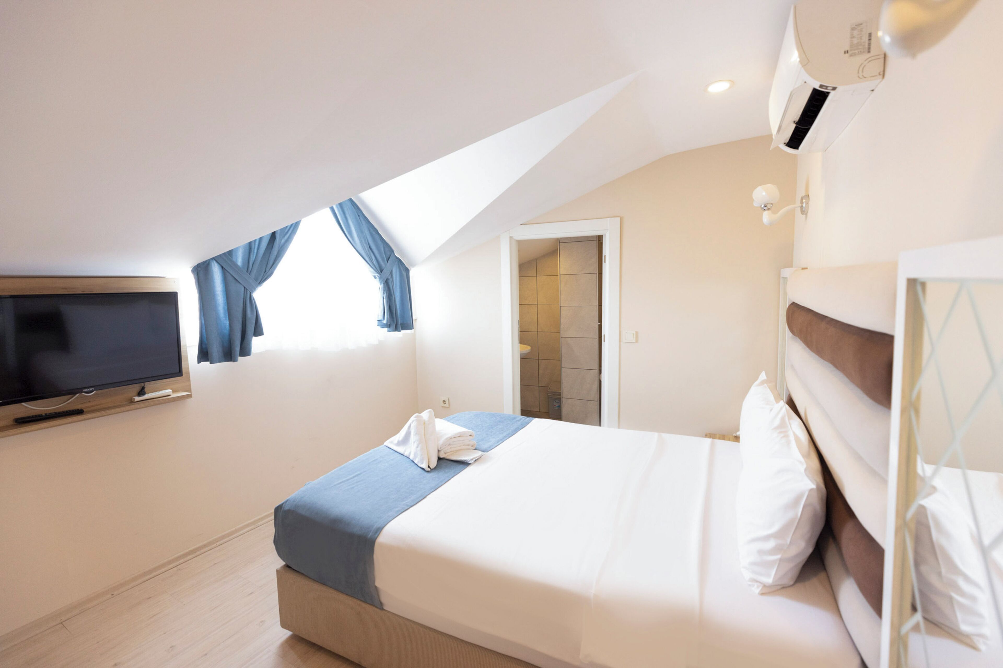Une chambre d’hôtel équipée d’un lit, d’une télévision, d’une fenêtre avec des rideaux et d’un appareil de climatisation.