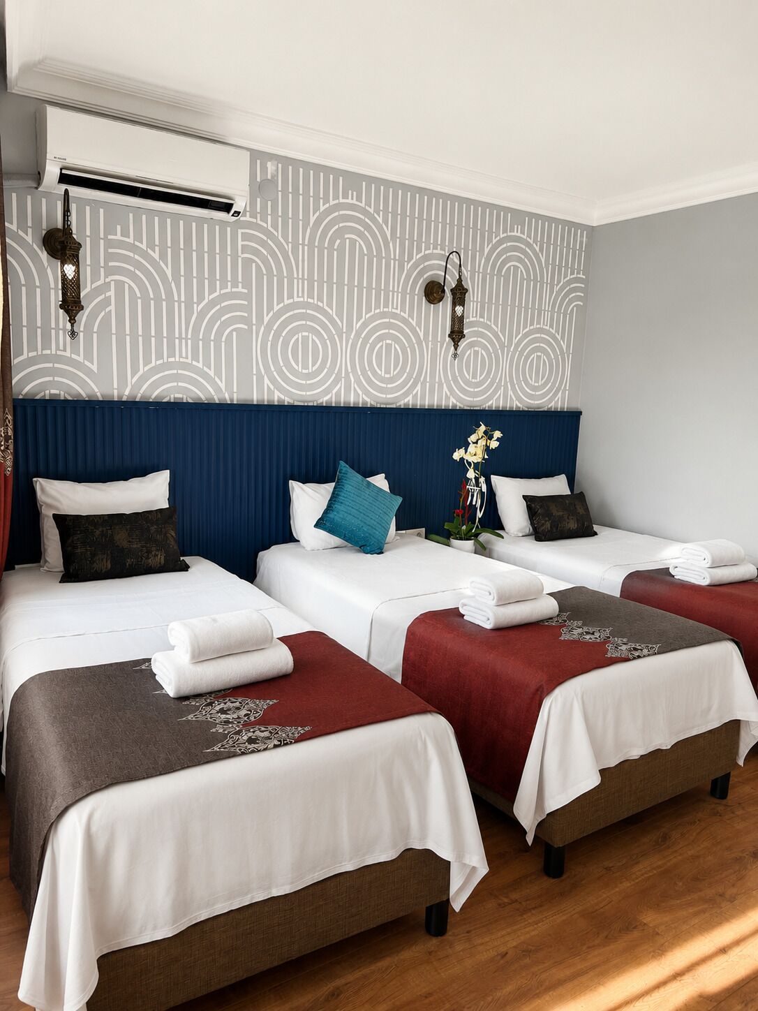 A hotel room with two beds, a blue headboard, a patterned wall, and an air conditioning unit.