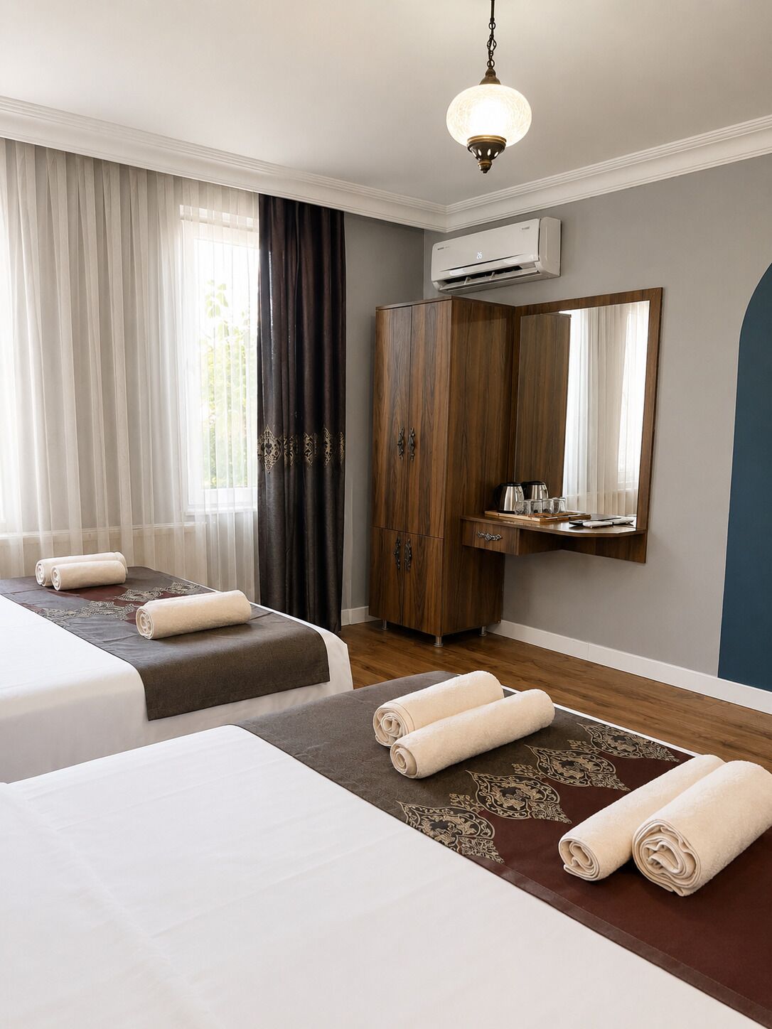 A hotel room with two beds, a wardrobe, a mirror, and an air conditioning unit.