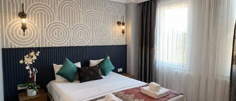 A hotel room with a large bed, a nightstand, a wall with a geometric pattern, a ceiling light fixture, and a window with curtains.