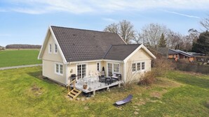 Ein zweigeschossiges Haus mit Terrasse, Treppe und Rasenfläche.