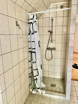 A shower with a white curtain featuring black geometric patterns, a handheld showerhead, and a wall-mounted faucet.